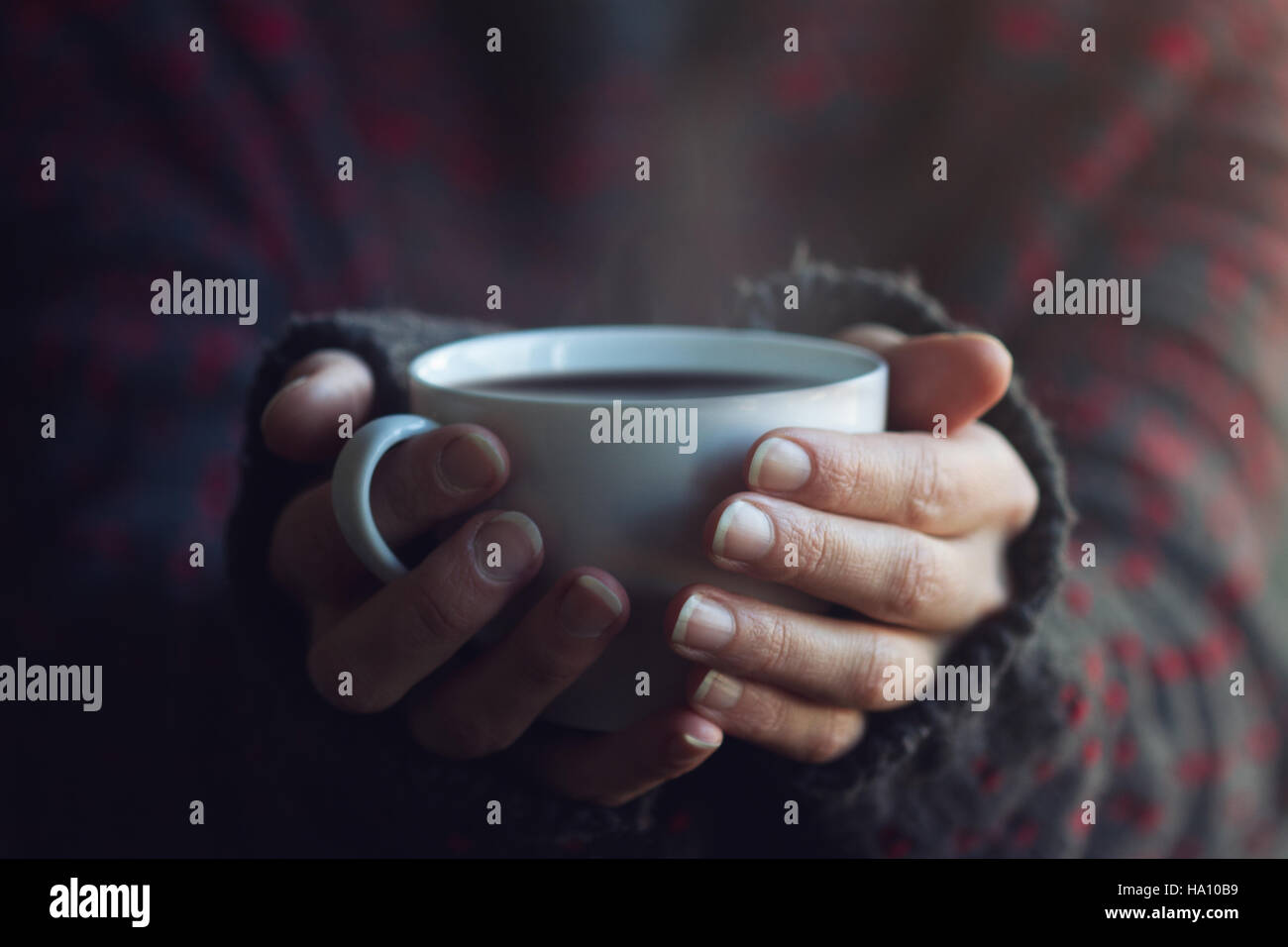 Woman in dark sweater hands holding a white cup of hot coffee with ...