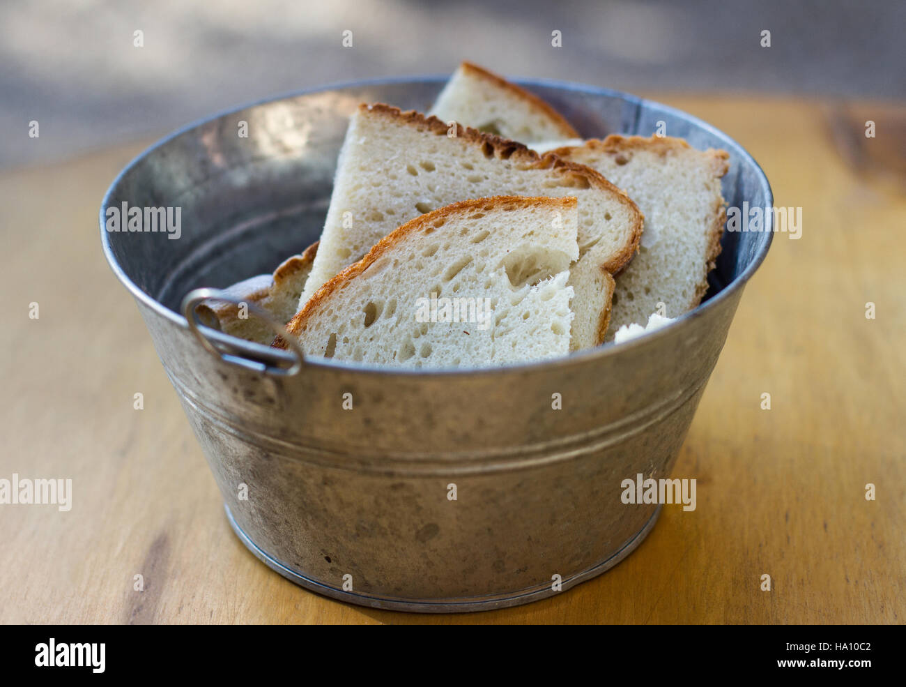 close up of aluminum bucket with handles and pieces of freshly cut bread standing on wooden board Stock Photo