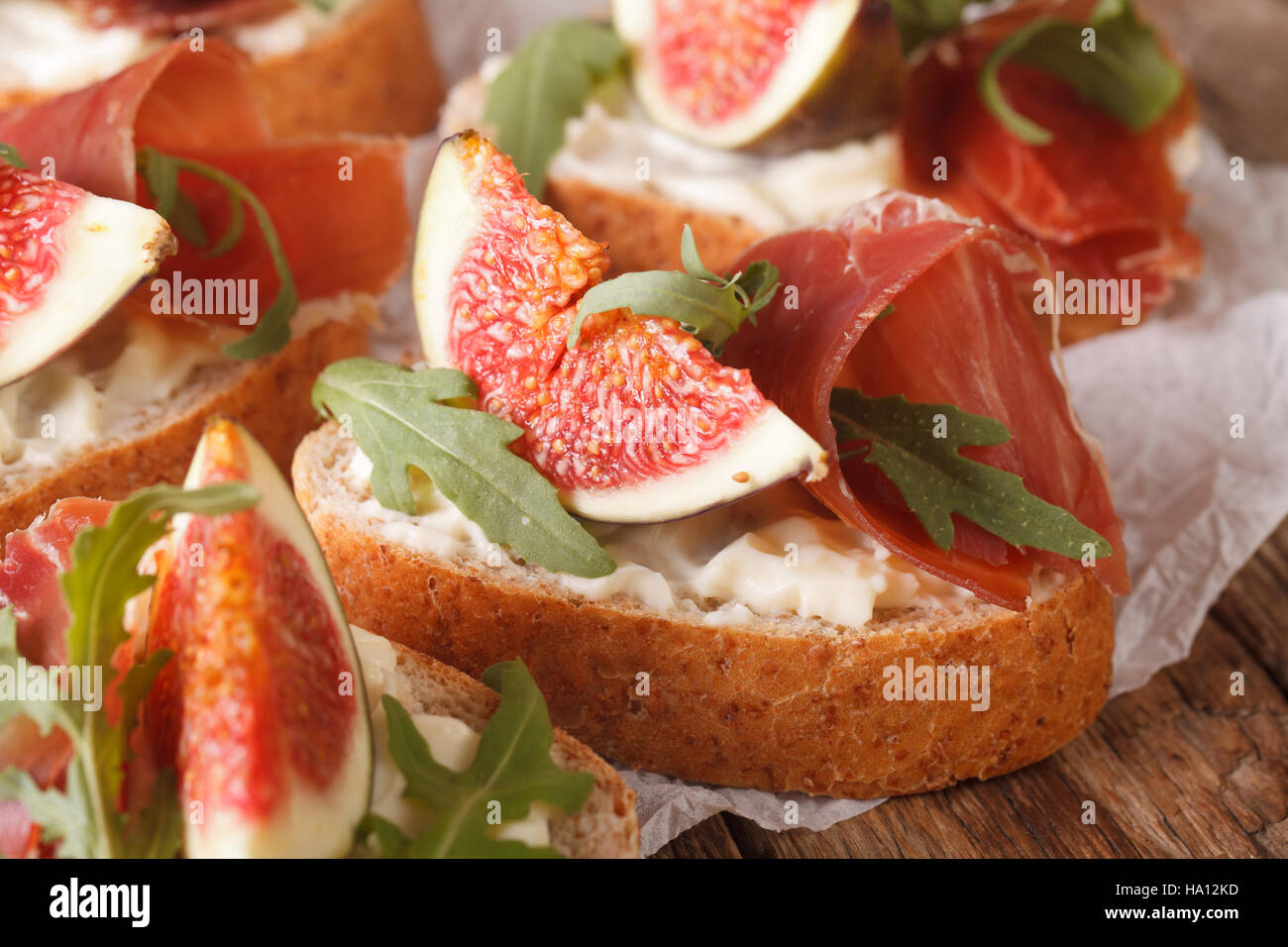 bruschetta with figs, prosciutto, arugula and cream cheese macro on the table. horizontal. rustic style Stock Photo