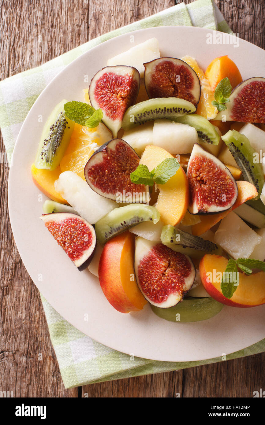 Sliced fresh fruit: figs, peaches, melons, kiwi and orange close-up on a plate. vertical view from above Stock Photo
