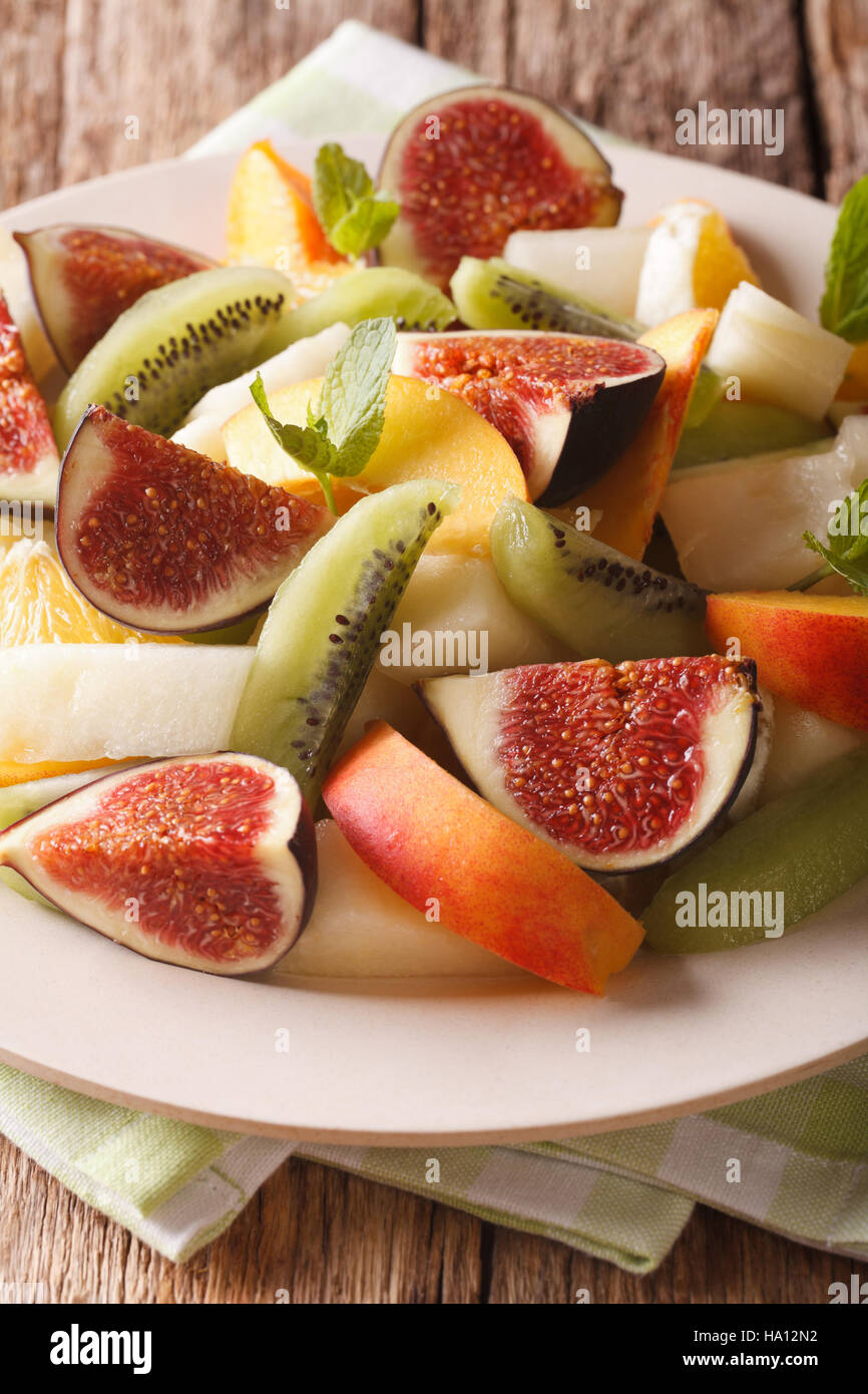 Fresh summer fruit salad with fig, peach, melon, kiwi and orange close-up on the table. Vertical Stock Photo