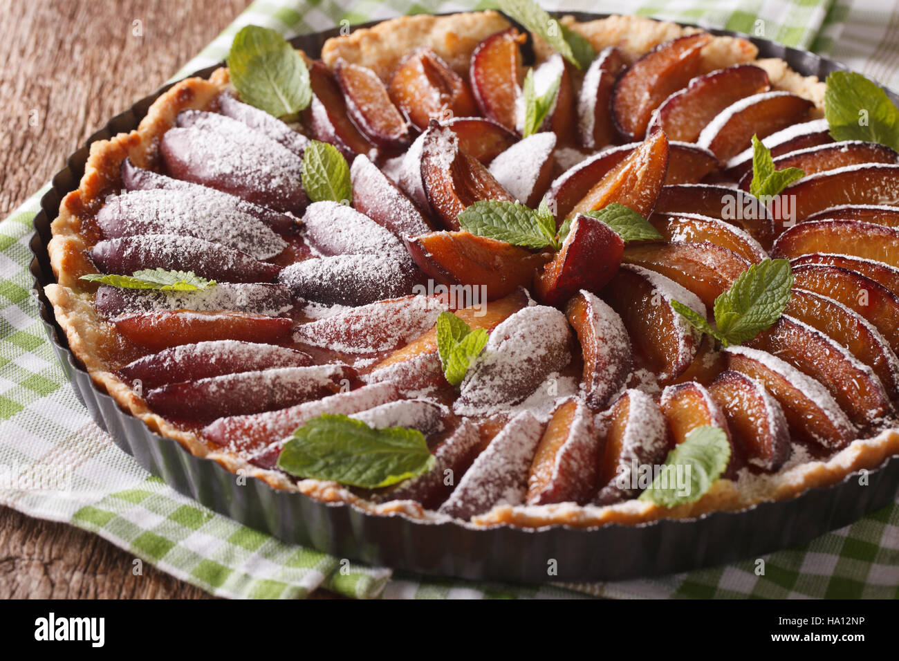 Delicious pastry plum tart with mint and powdered sugar closeup on