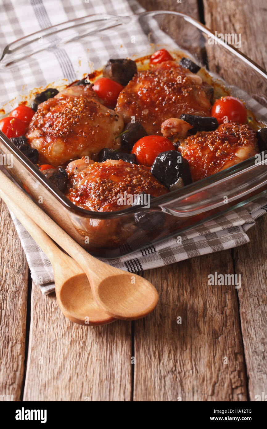 Baked chicken thigh with mustard, tomatoes and wild mushrooms close up in baking dish on the table. Vertical Stock Photo