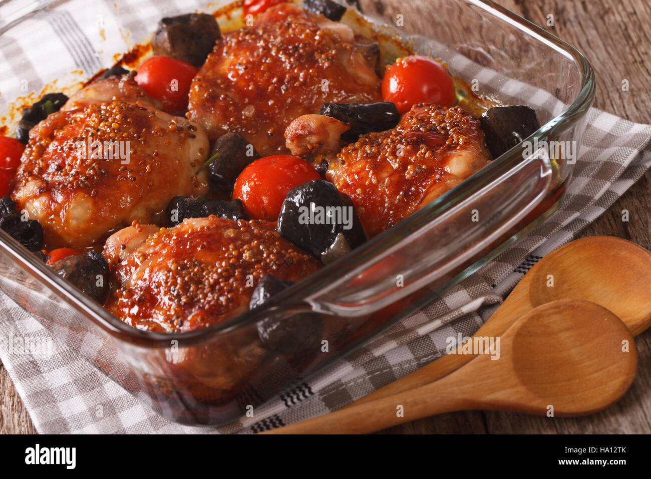 Baked chicken thigh with mustard, tomatoes and wild mushrooms close up in baking dish on the table. horizontal Stock Photo