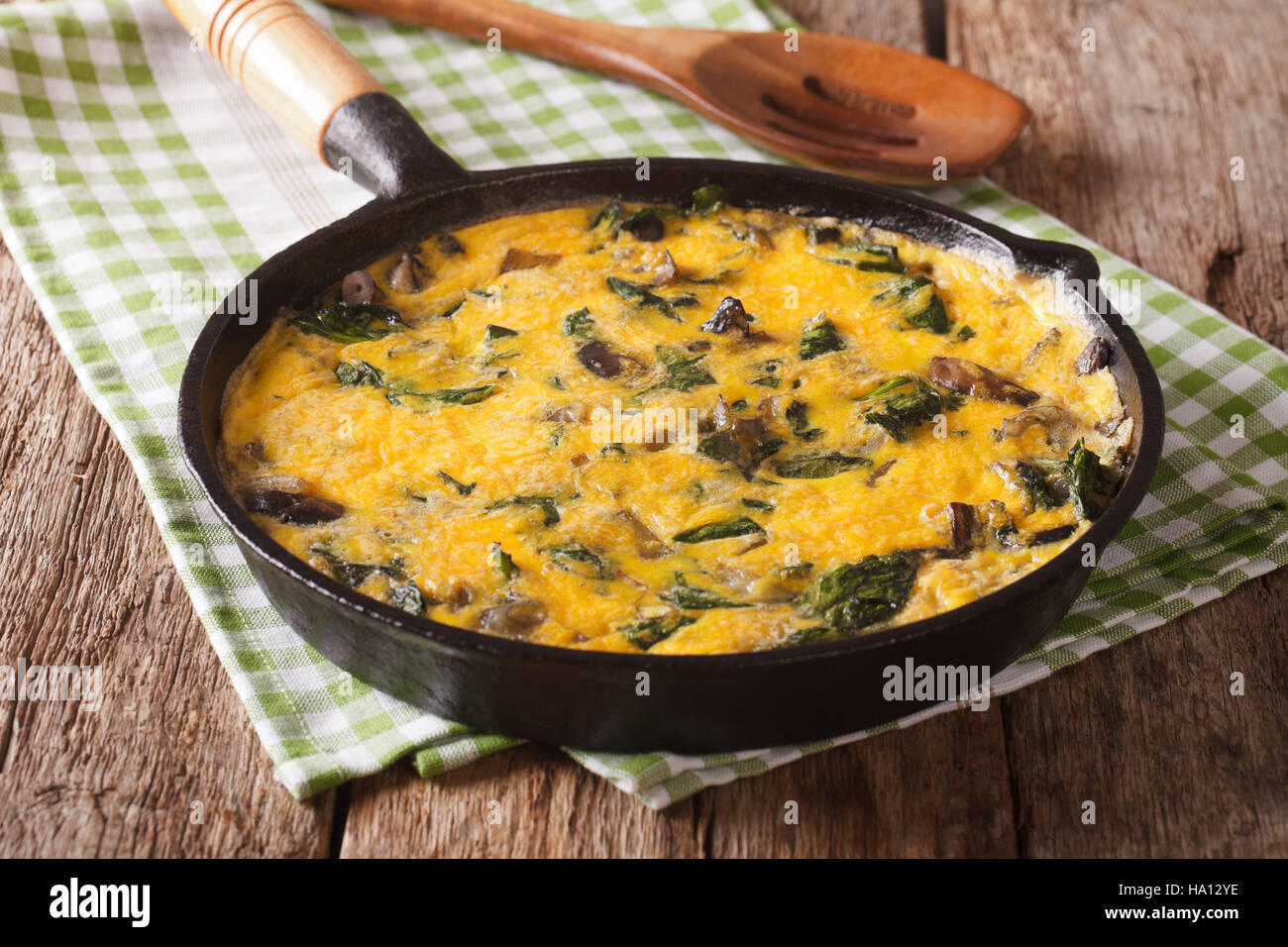 Hot scrambled eggs with spinach, cheddar cheese and mushrooms in a frying pan close-up on the table. horizontal Stock Photo