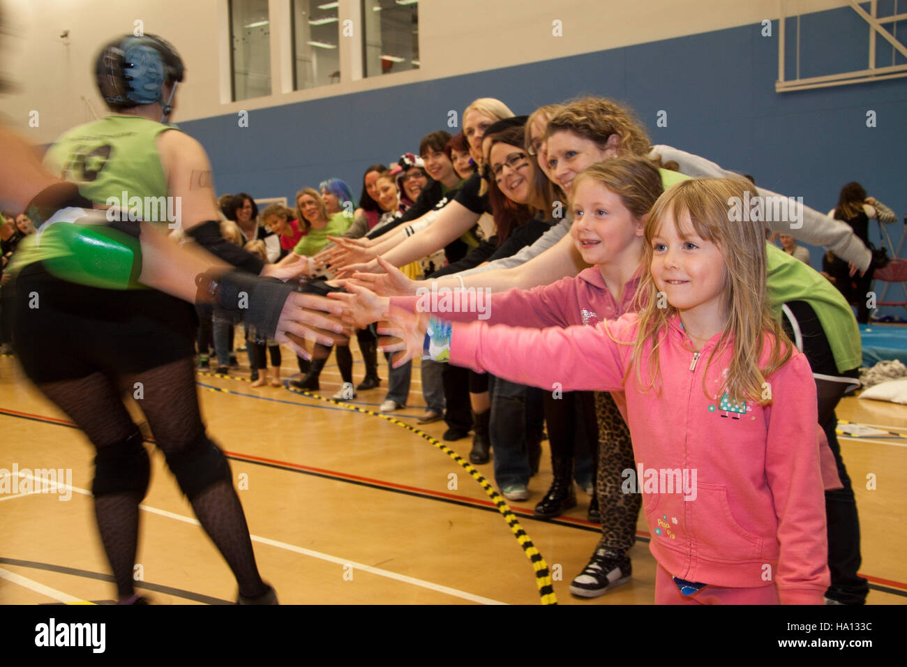 Two young girls in pink at the front of a roller derby high five line Stock Photo