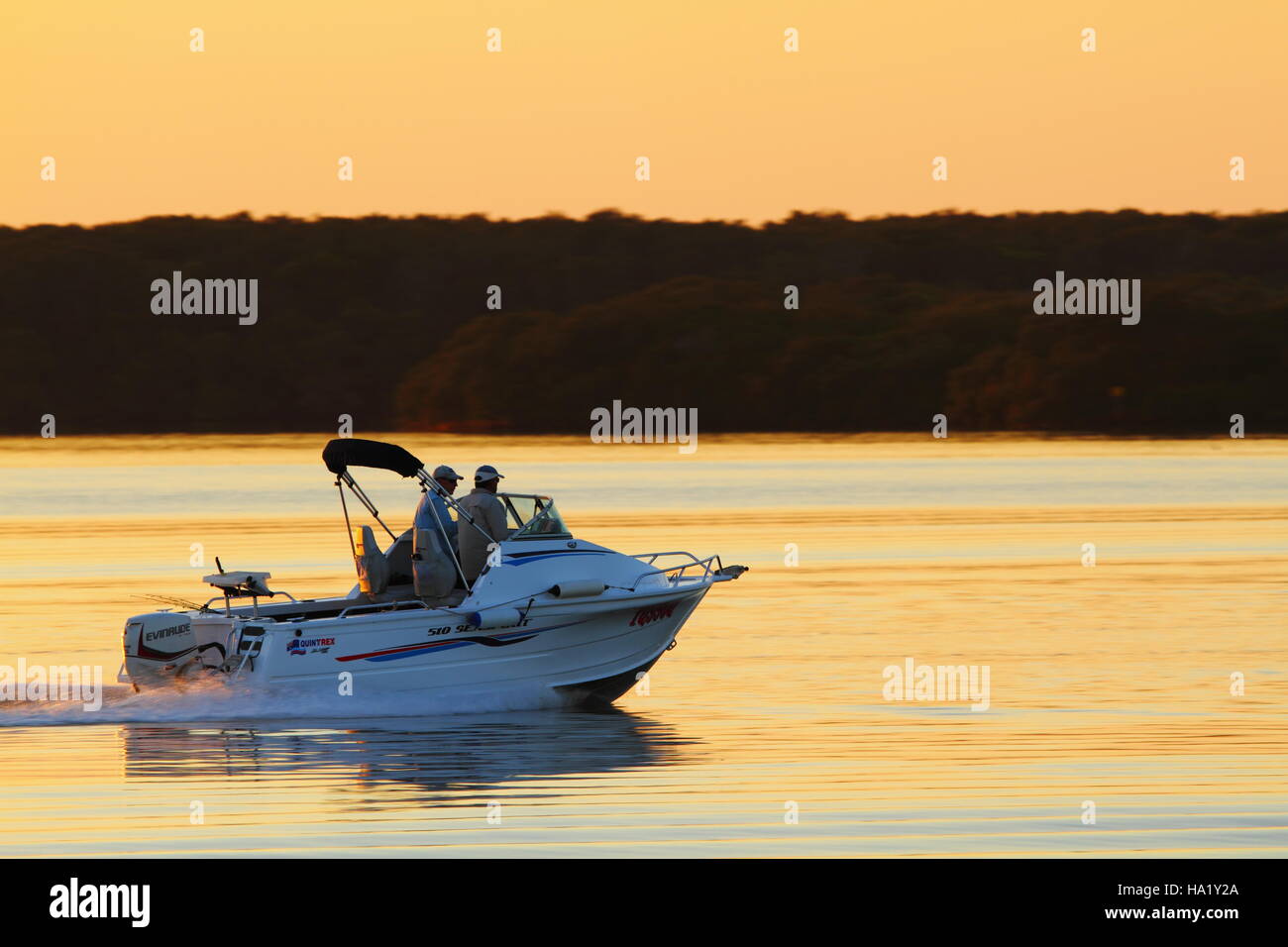 Dawn greets two men on a boat on Pumicestone Passage off Golden Beach, Caloundra on the Sunshine Coast of Queensland, Australia. Stock Photo