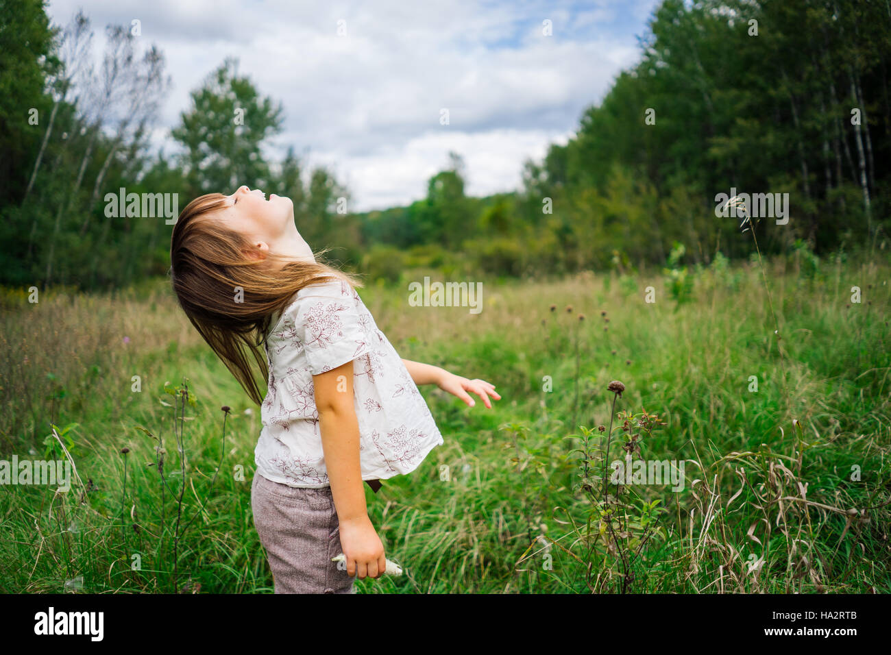 Girl standing in field throwing her head back laughing Stock Photo