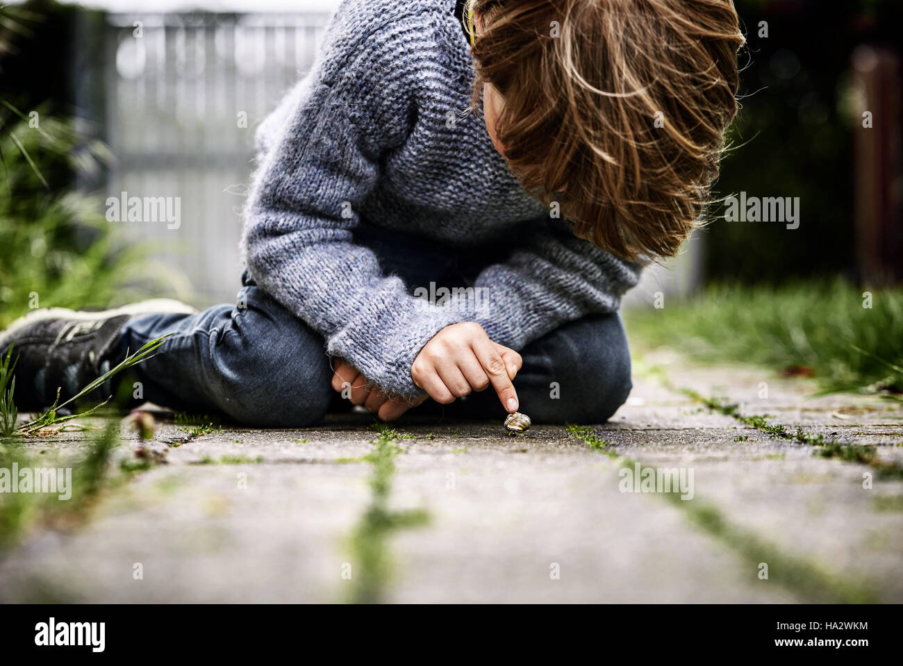 Boy sitting on ground looking at a snail Stock Photo