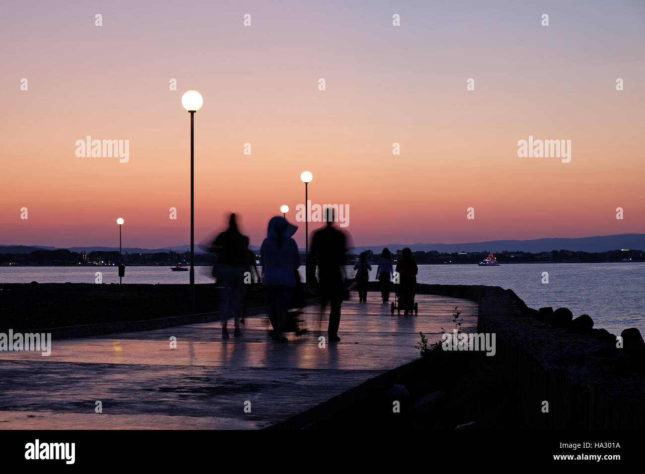 Silhouettes of people walking near sea on sunset background Stock Photo ...