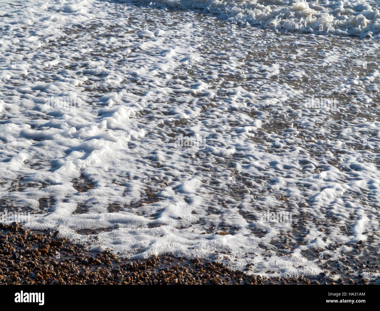 Close up of foam and froth on a pebble beach during rough seas Stock Photo