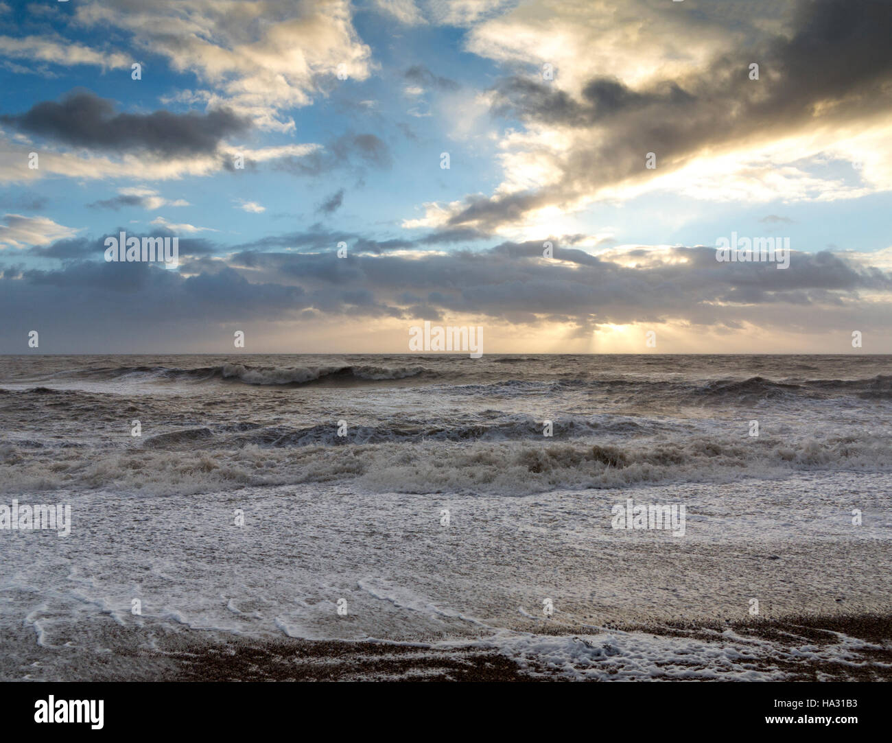 Churning waves breaking on the shoreline during heavy winds and spray with foam in the foreground just after sun rise. Stock Photo