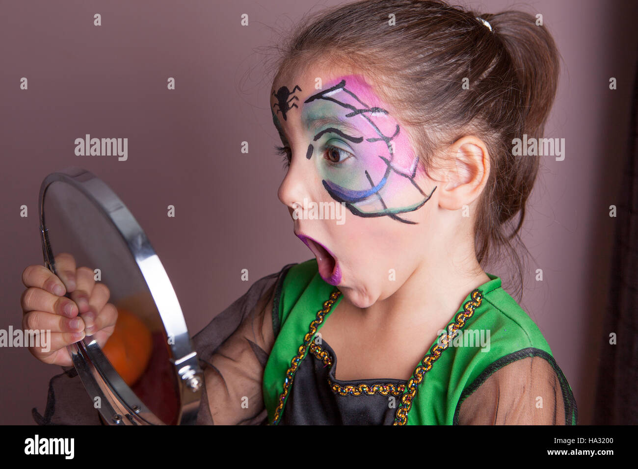 Little girl looking surprised into the mirror after face painting session before halloween party Stock Photo