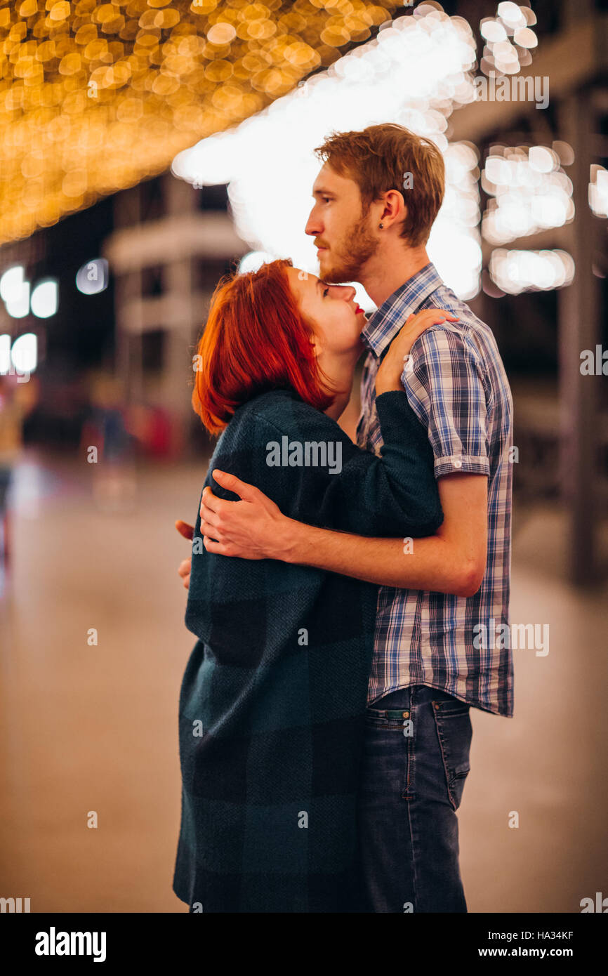 Happy couple embracing and kissing in the evening on a light garlands ...