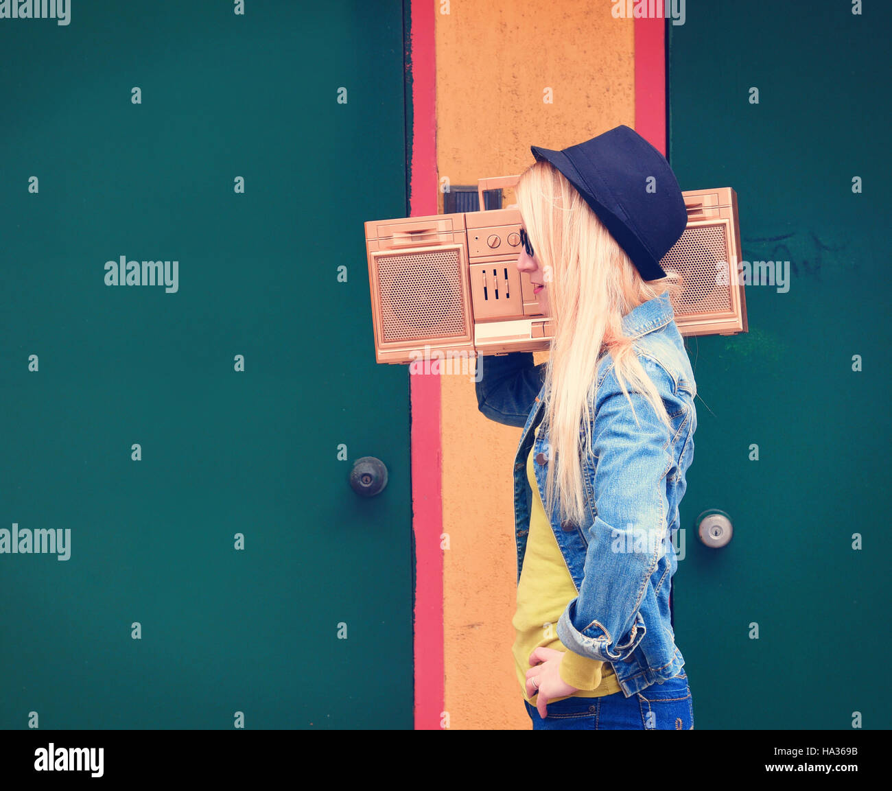 A blond hipster girl with glasses is listening to a vintage gold boombox radio with a speaker for a music entertainment concept. Stock Photo