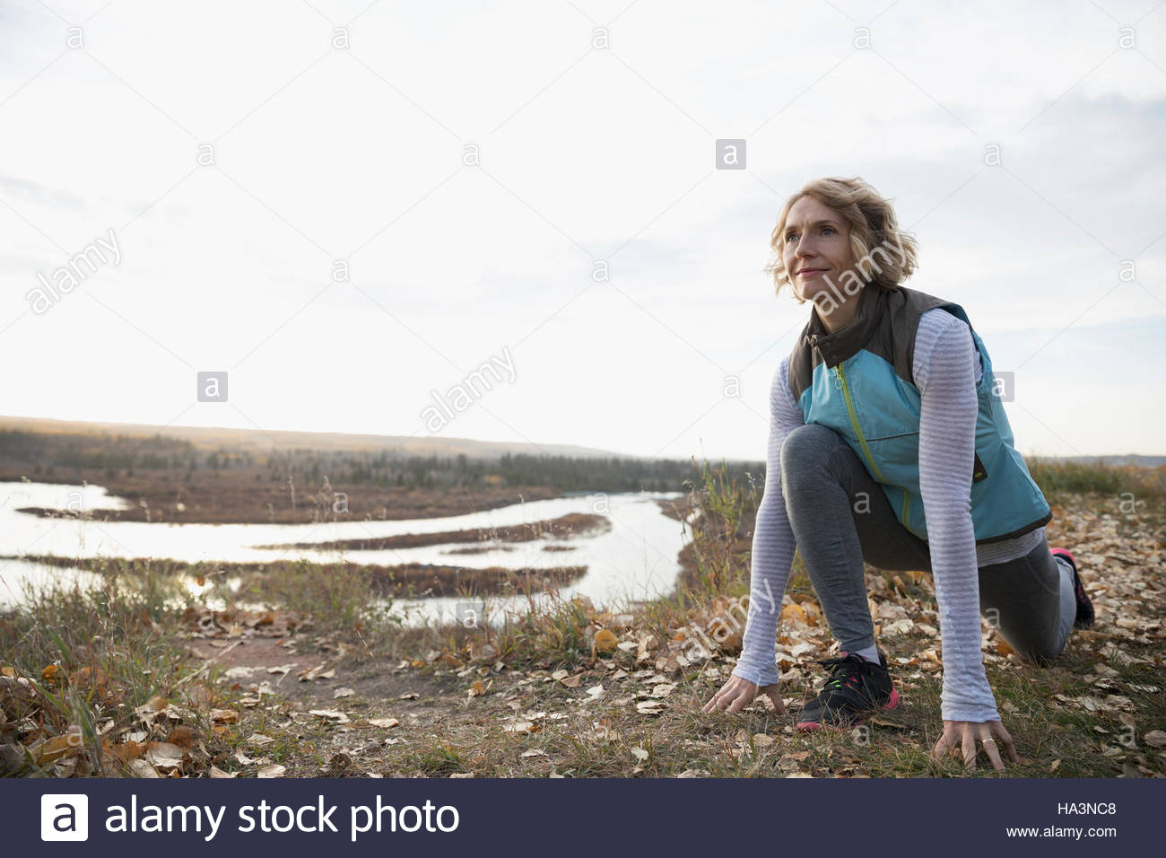 Woman practicing yoga low lunge on autumn hilltop overlooking lake Stock Photo