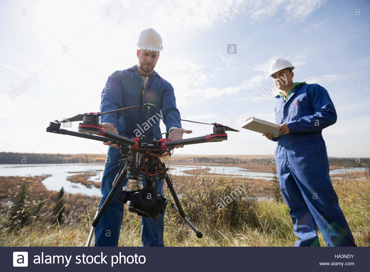 Surveyors with drone equipment on sunny hilltop overlooking lake Stock