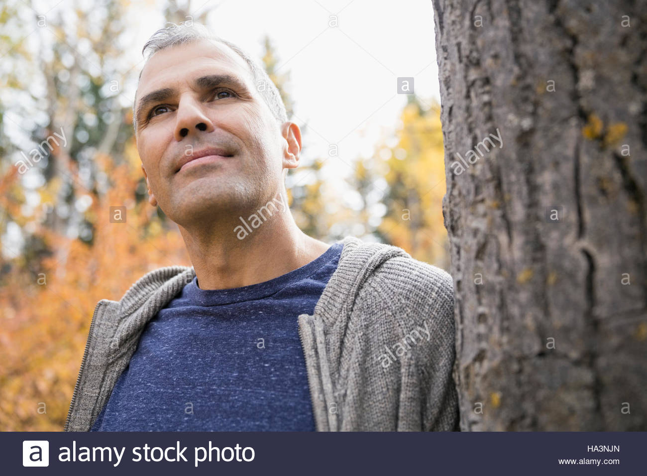 Pensive man leaning on tree trunk looking away Stock Photo