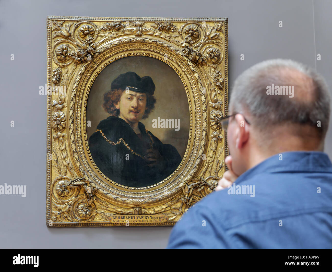 Tourist admiring a painting of Rembrandt - Self-Portrait Wearing a Toque and a Gold Chain exhibited at the Louvre Museum Stock Photo