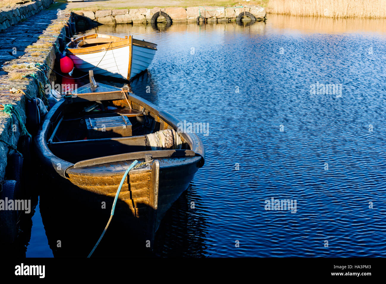 Cold morning with small wooden fishing boats moored beside a stone pier in fall. Copy space. Stock Photo