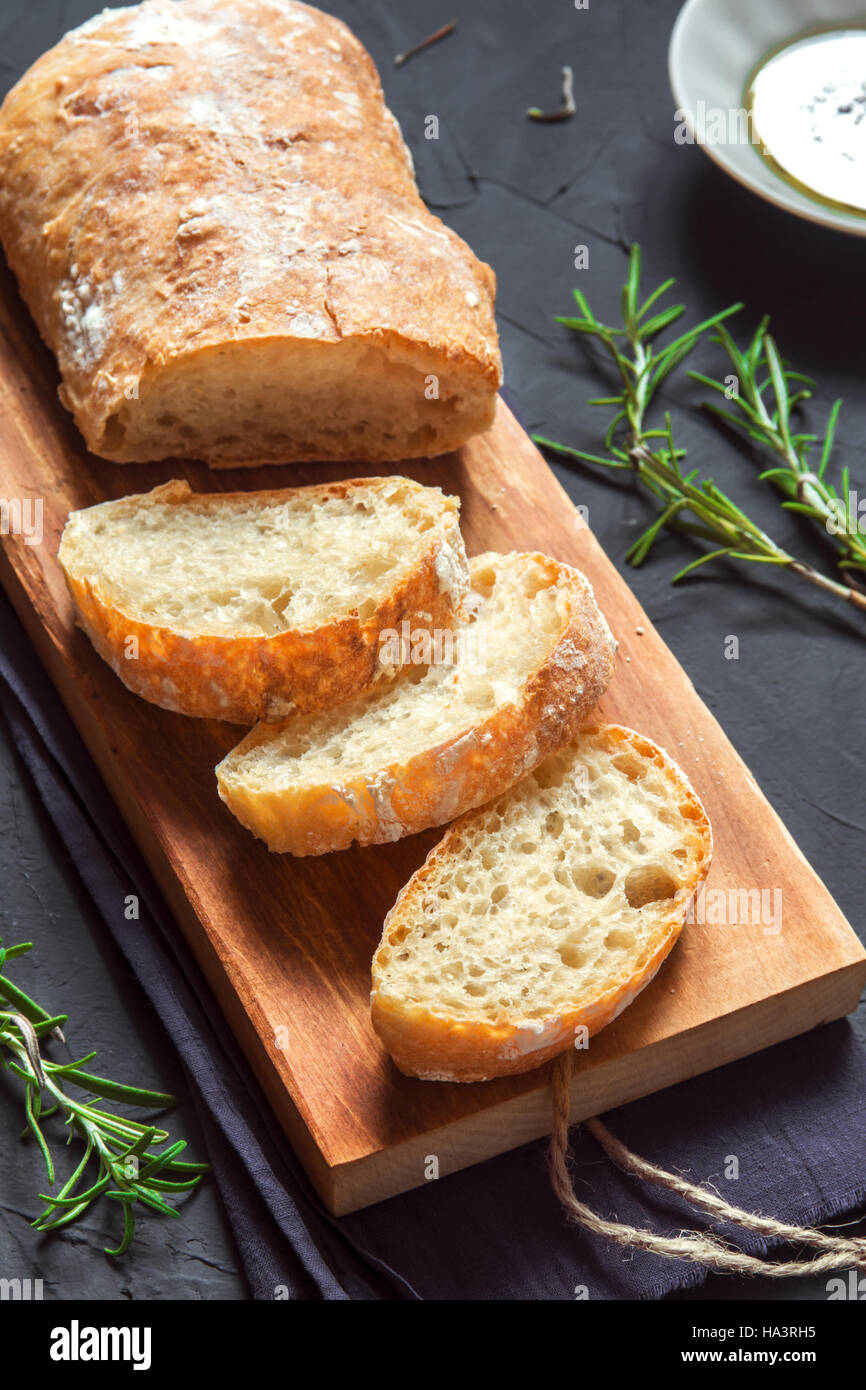 Italian bread Ciabatta and rosemary on black background - fresh homemade bread bakery Stock Photo