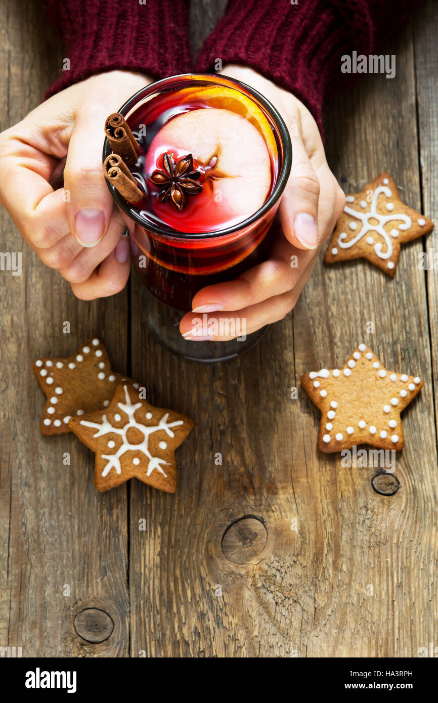 Christmas hot drink - mulled wine in female hands with cinnamon stick, star anise and festive Christmas gingerbread cookies over rustic wooden backgro Stock Photo