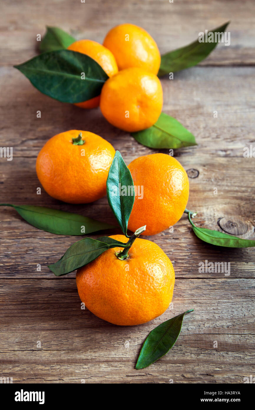 Tangerines (mandarins, clementines, citrus fruits) with leaves over rustic wooden background