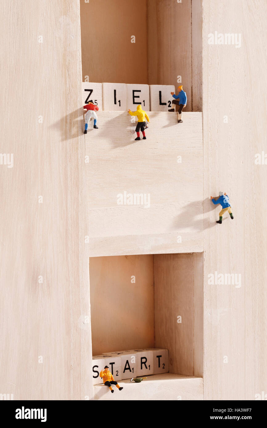 Miniature mountain climbing figures, climbing between wooden blocks with lettering that spell from start to ziel Stock Photo