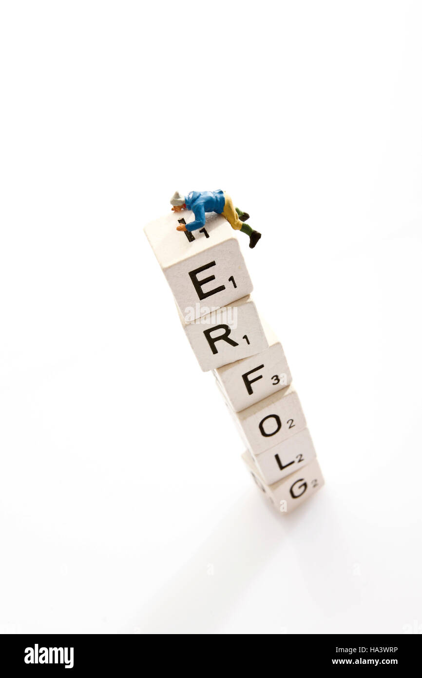 Lettered dice which spell Erfolg, German for Success, and a miniature mountain climber figure Stock Photo