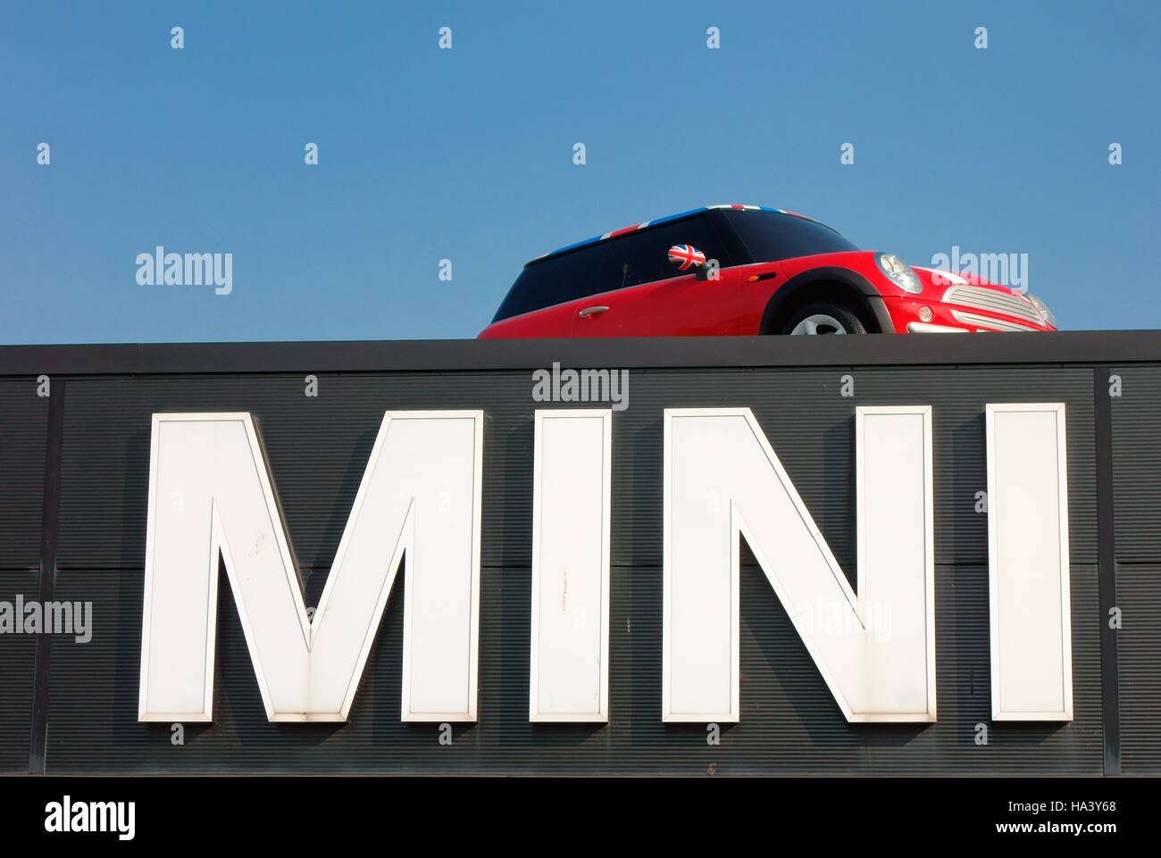 Mini car on a roof above giant mini sign Stock Photo