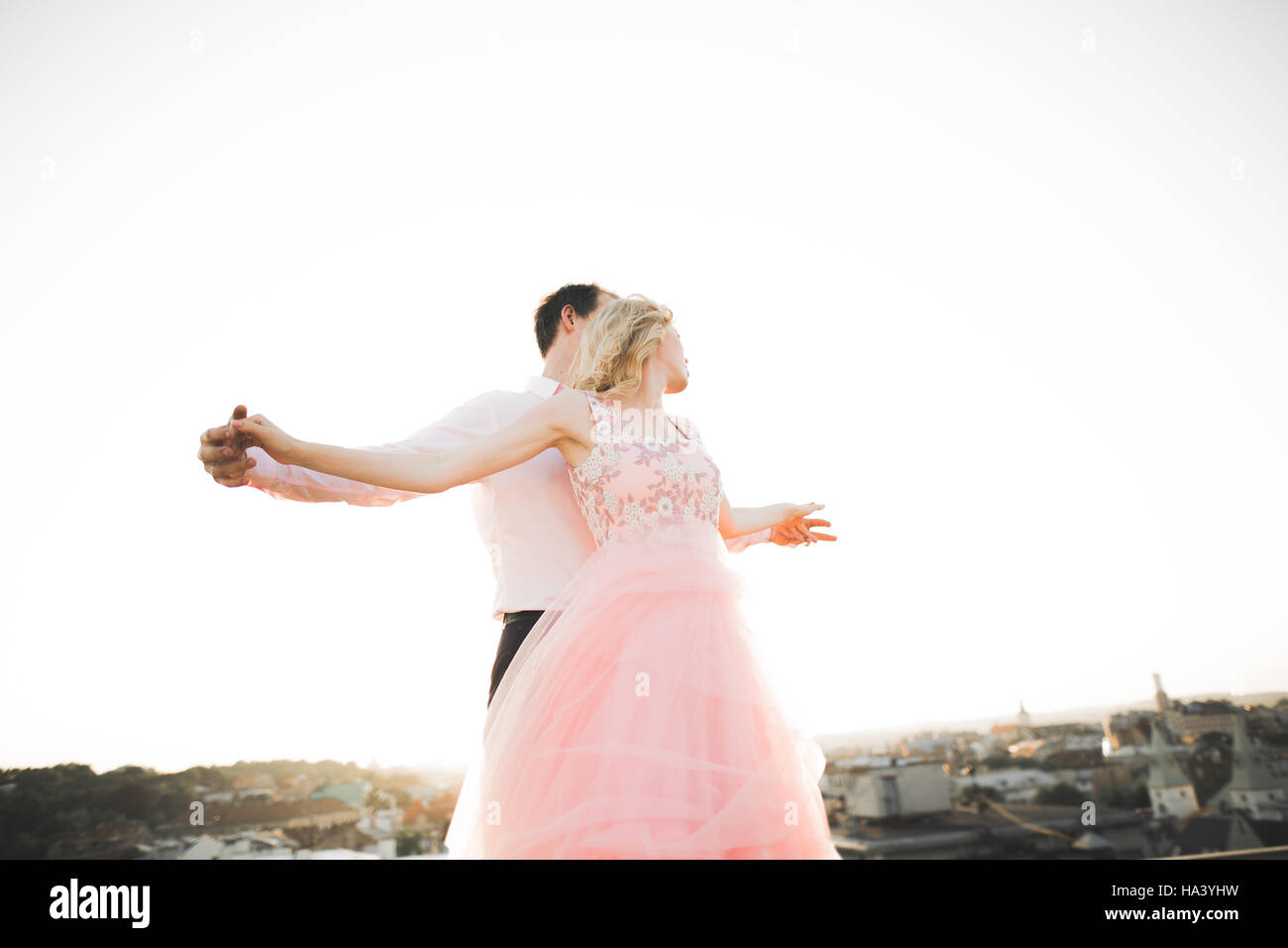 Young couple in love posing on roof with perfect city view holding hands and hugging . Beautiful sunset Stock Photo