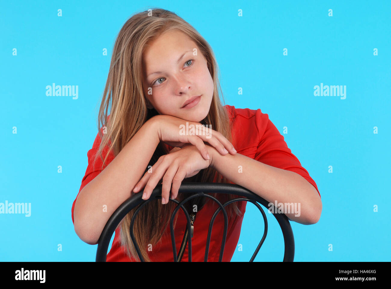 Smiling girl sits on a chair isolated on blue Stock Photo - Alamy