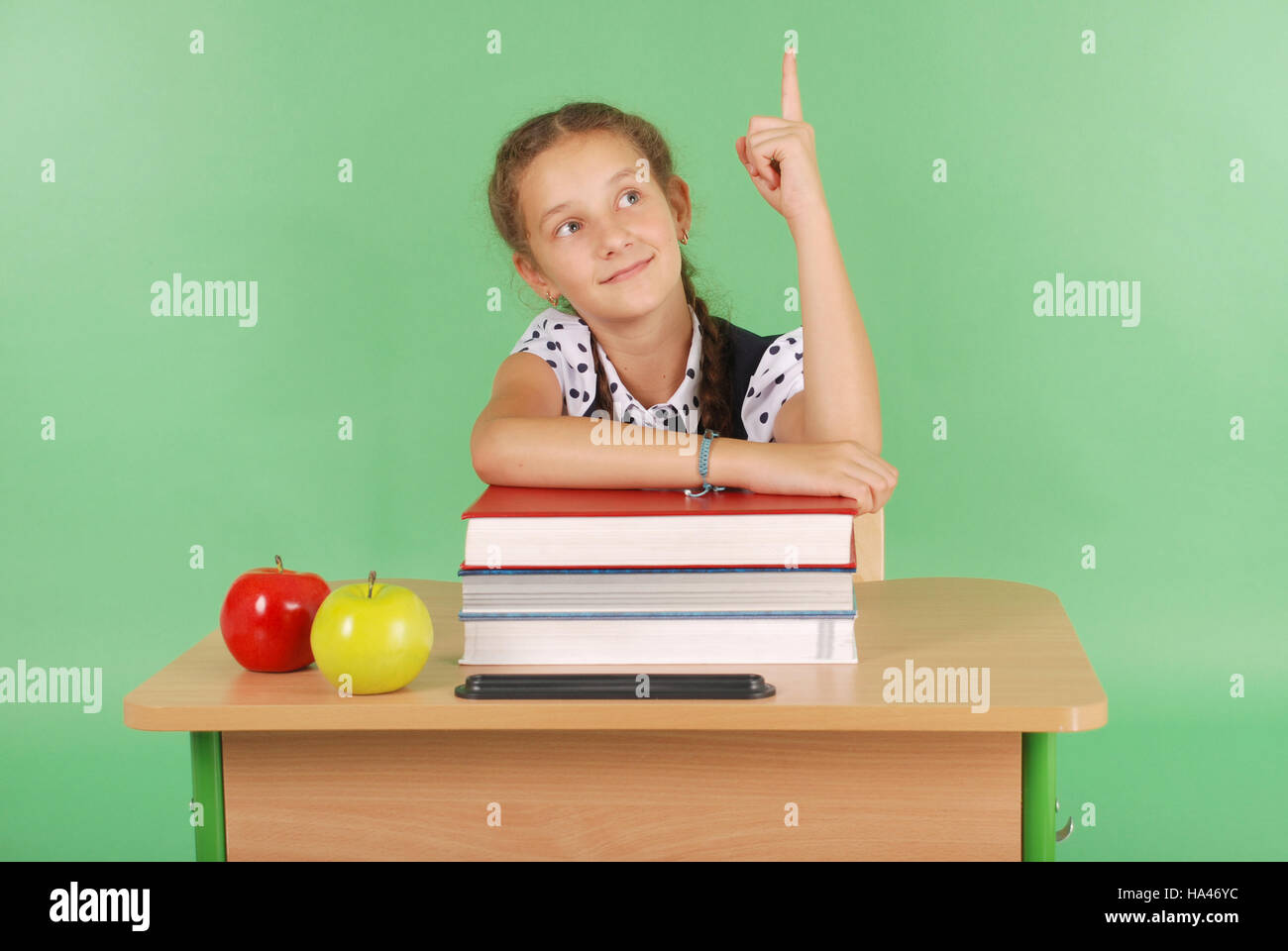 Girl in a school uniform raising hand to ask question isolated on green