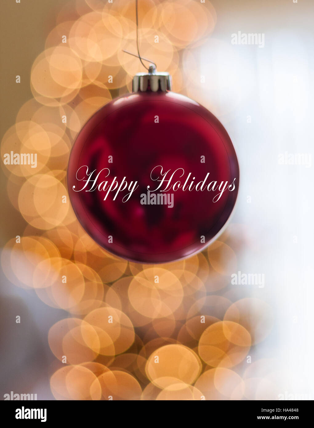 Single Red Happy Holidays Ornament hanging in front of lights Stock Photo