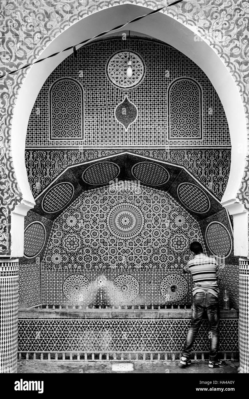 A Young Man Collects Water From A Public Water Fountain In The Medina, Fez el Bali, Fez, Morocco Stock Photo