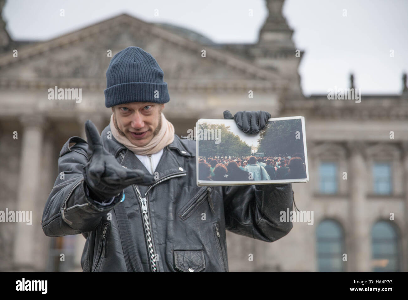 Berlin, Deutschland. 19th Nov, 2016. Stadtführer Philipp führt die Teilnehmer beim Bowie Walk am 19.11.2016 in Berlin vor den Reichstag und zeigt ein Foto, das Bowie-Fans auf der Ostseite der Berliner Mauer zeigt. Foto: Jörg Carstensen/dpa/Alamy Live News Stock Photo