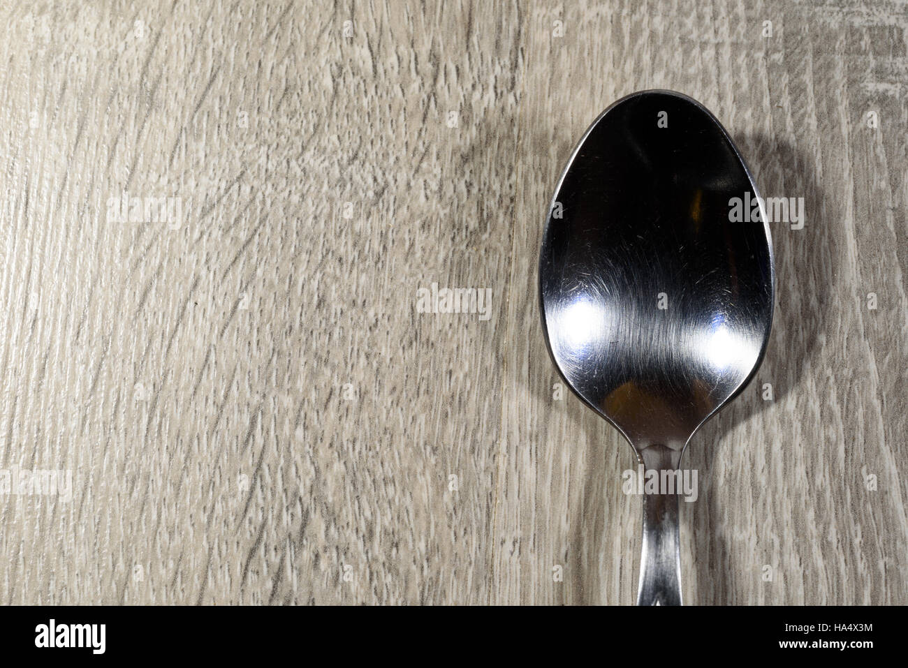 Single shiny empty silver spoon on a wooden kitchen background Stock Photo