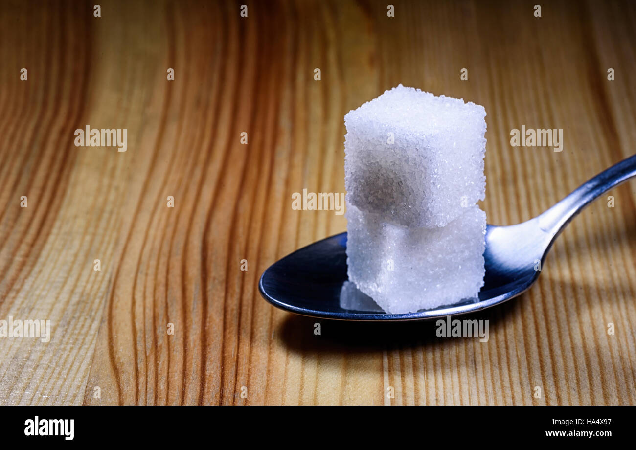 Two sugar spoon lumps resting on a silver teaspoon on a wooden textured