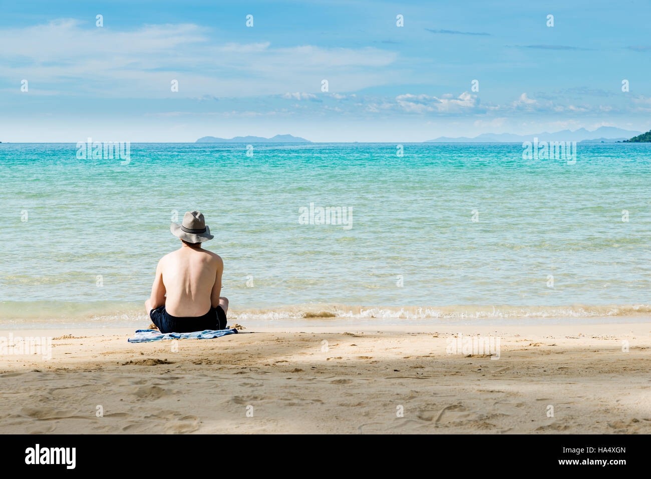 Asian man on beach rear view guy wearing summer hat, sitting looking to sea blue sky, summer travel vacation concept of freedom travel beach sea. Stock Photo