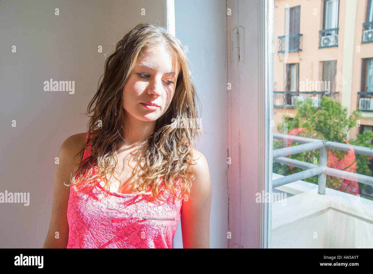 Young woman leaning against the wall and looking through the window. Stock Photo