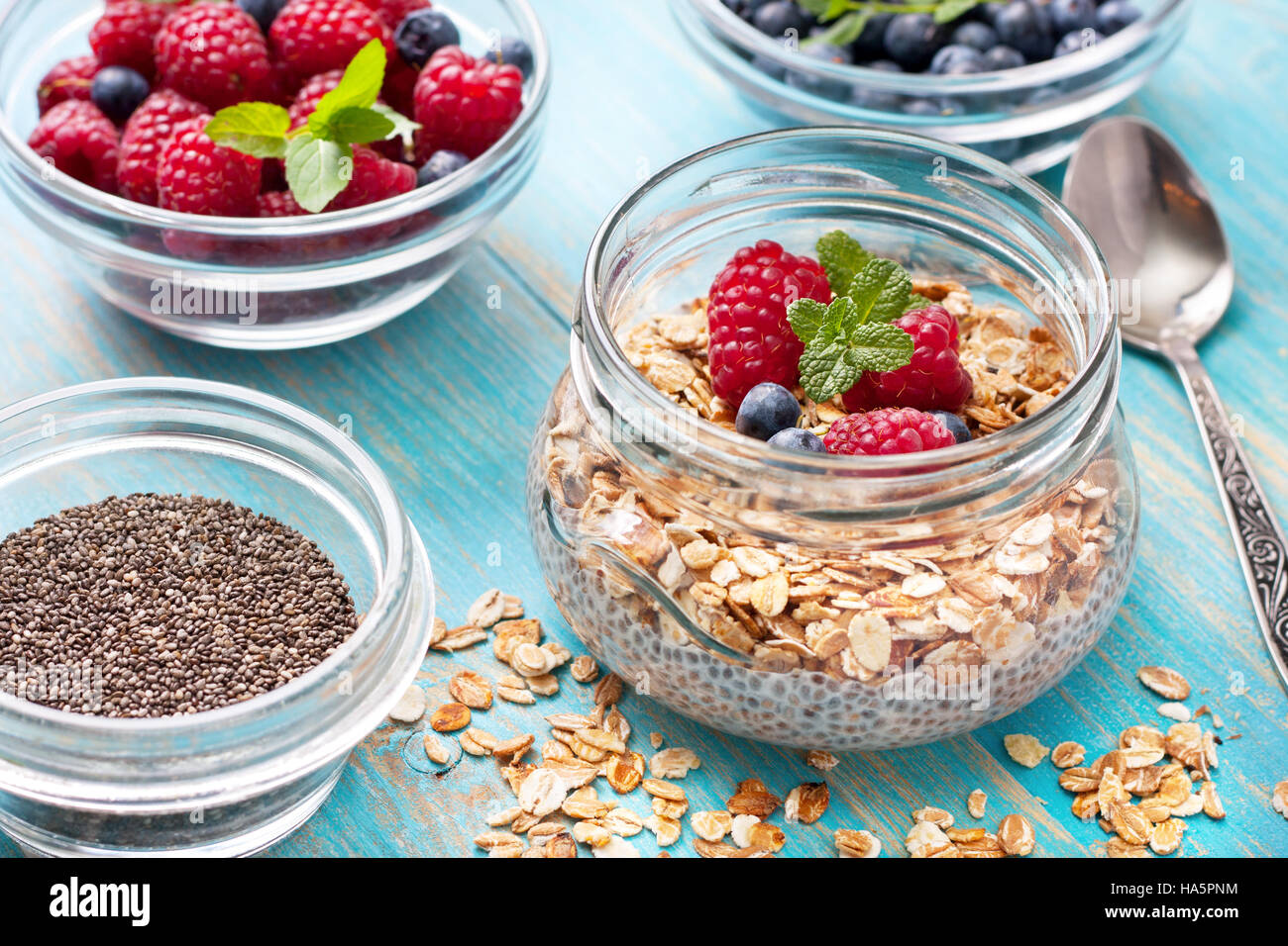 Healthy dietary breakfast. Chia pudding with muesli, raspberries, blueberries in a glass bowl, fresh berries on blue wooden background Stock Photo