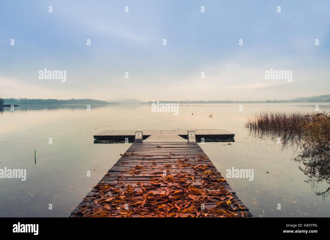 Wooden pier with leaves on the quiet lake in autumn Stock Photo