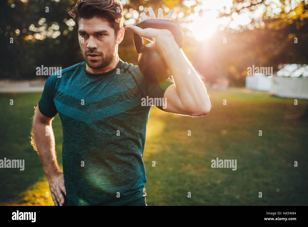 Shot of fit young man exercising with kettlebell in the park.  Strong young guy training at park in morning. Stock Photo