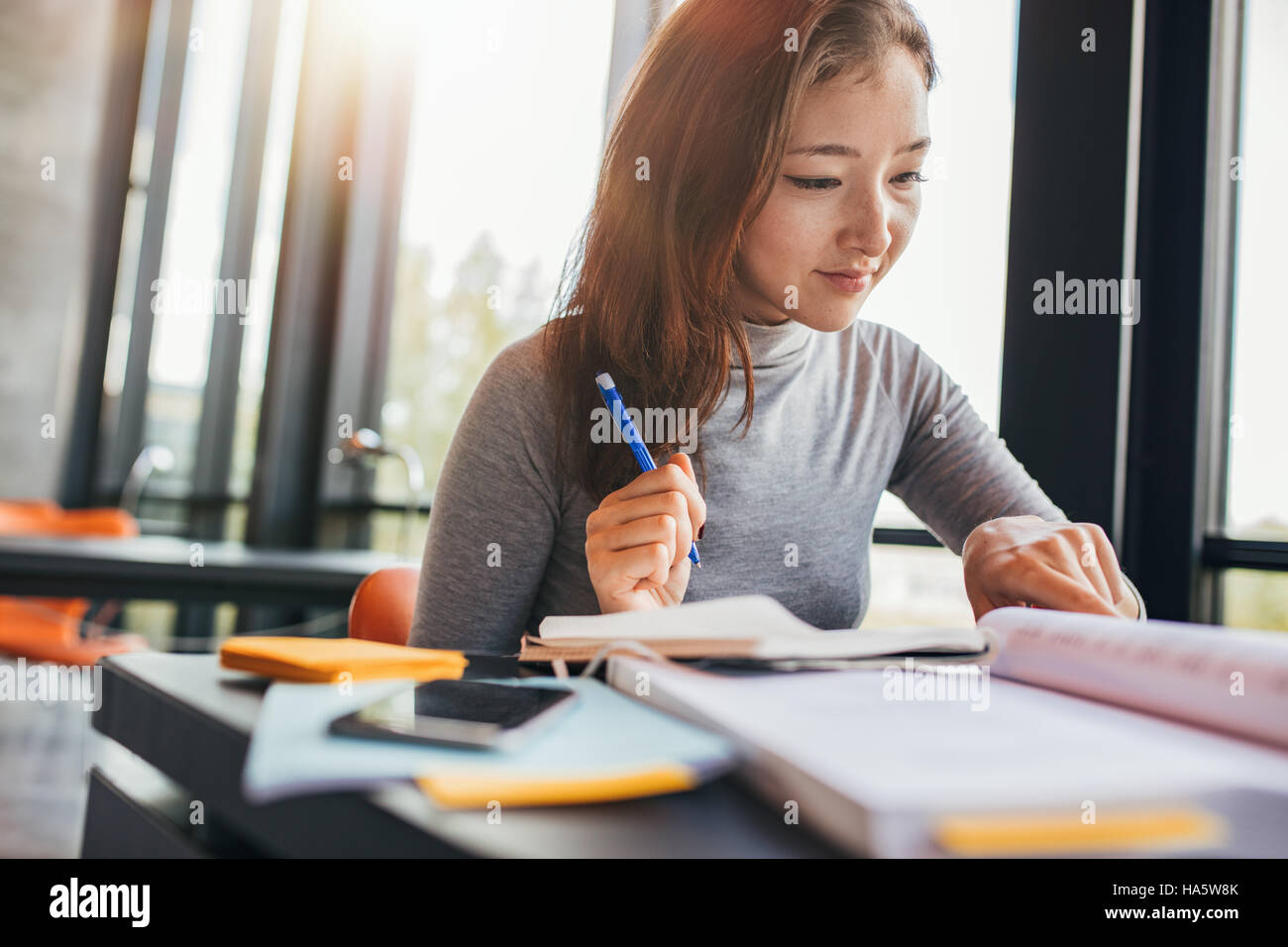 Young asian woman reading book in university library. Female student preparing for final exams. Stock Photo