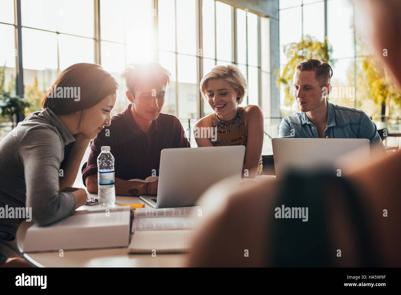university students sitting together at table using laptop in class. Young people working on laptop in library. Stock Photo