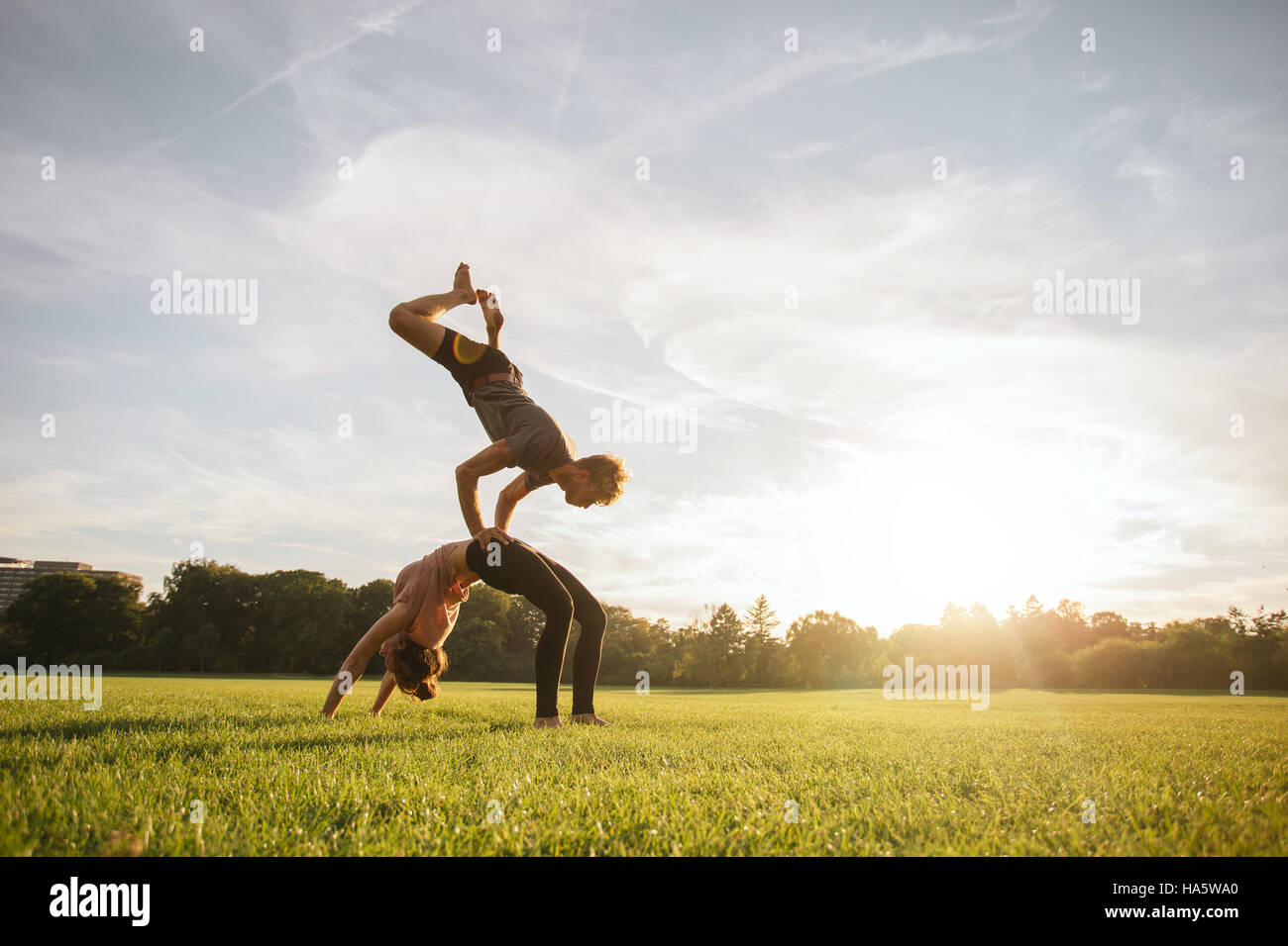 Healthy young couple doing acro yoga on grass. Man and woman doing various yoga poses in pair outdoors at the park. Stock Photo