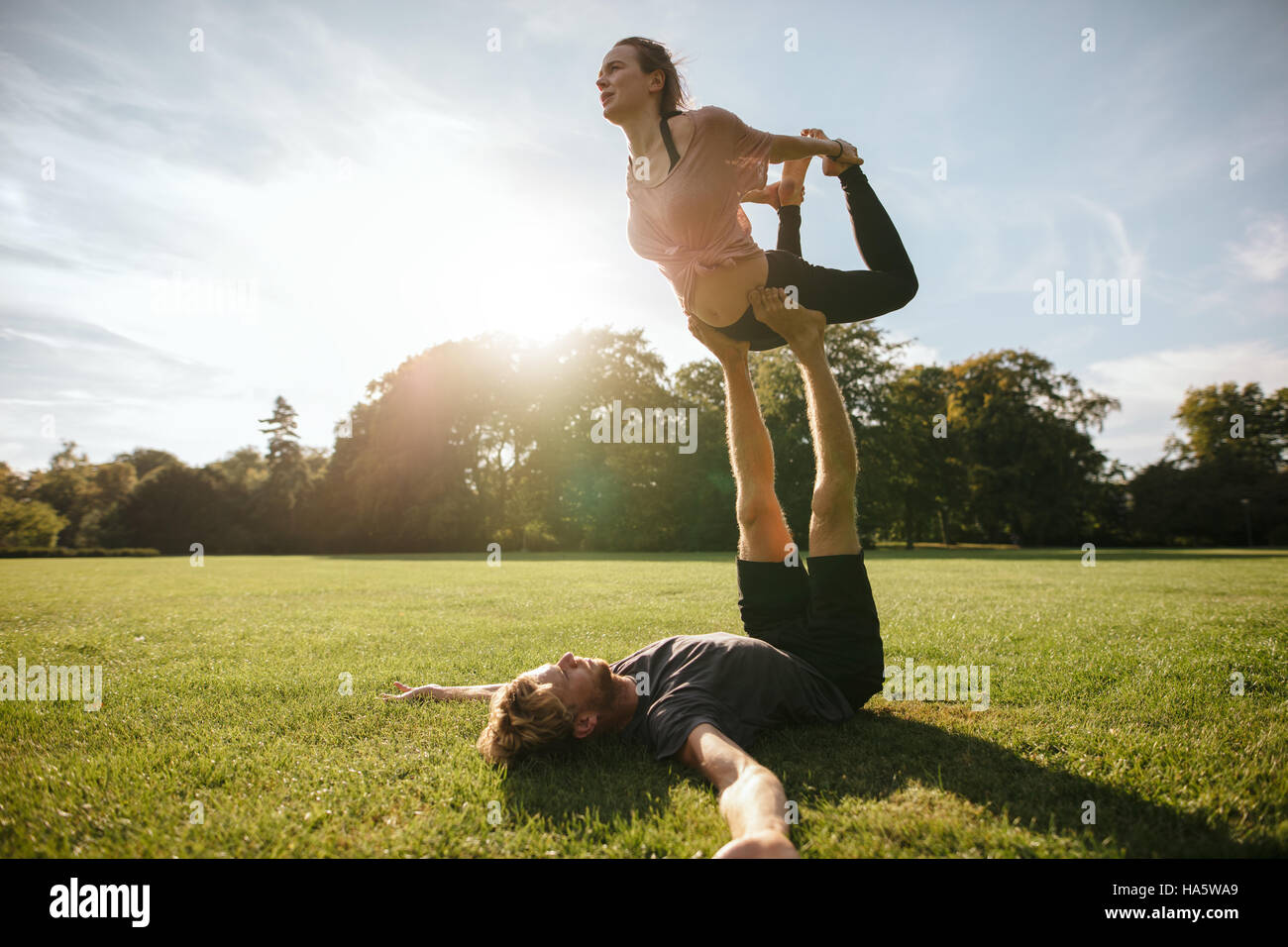 Healthy young couple doing acro yoga on grass. Man and woman doing various yoga poses in pair outdoors at the park. Stock Photo