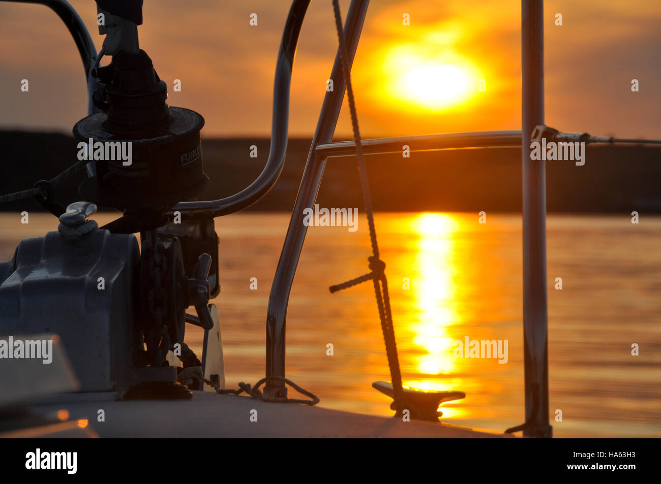 Sunset from a yacht at anchor looking past the anchor windlass and foredeck fittings Stock Photo