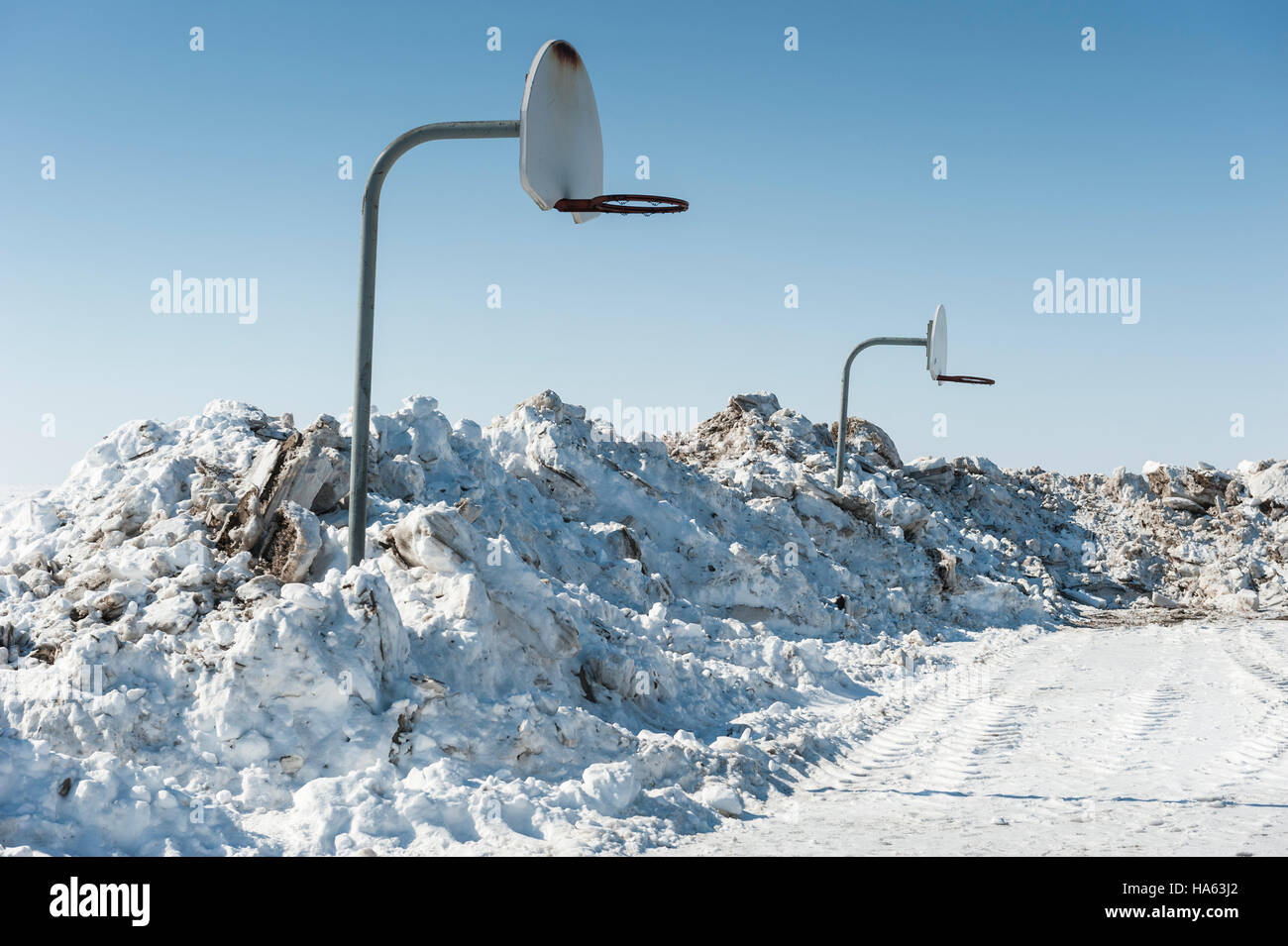 Two basketball nets in winter surrounded by piles of shoveled snow in
