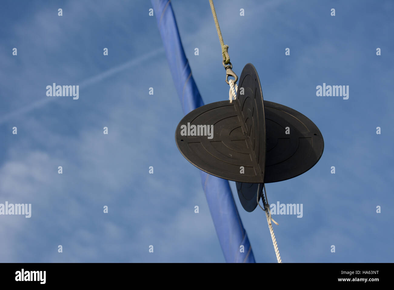 Anchor ball in yachts rigging with rolled blue foresail against a blue sky with white clouds Stock Photo